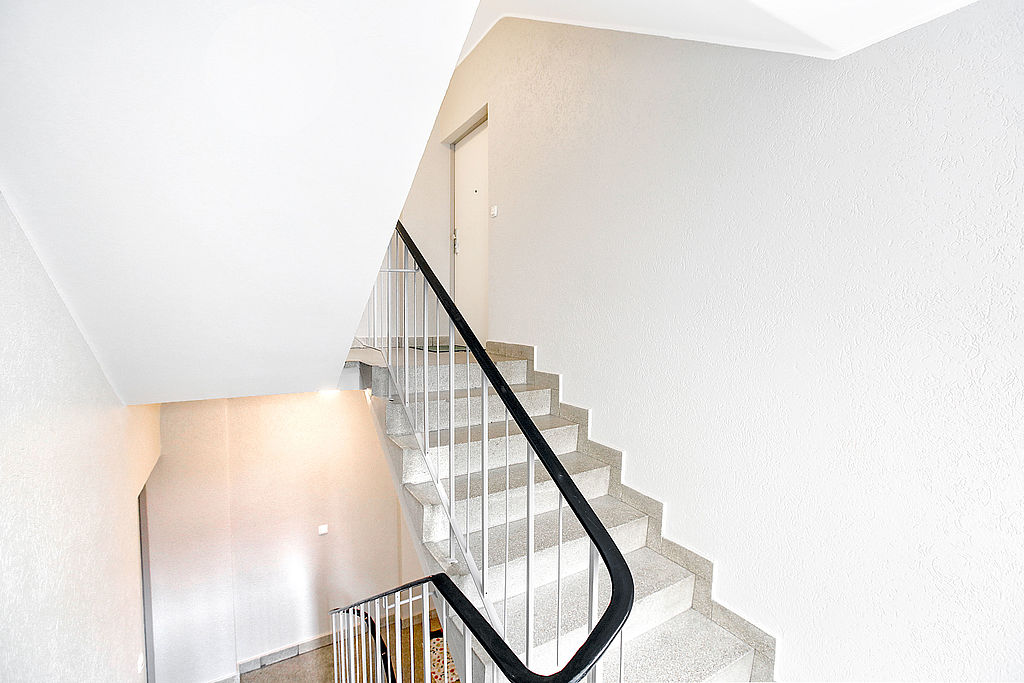 Renoviertes Treppenhaus mit weißem Anstrich und schwarzem Handlauf